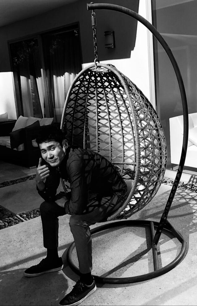 Trevor Zhou A black and white photo of Trevor Zhou seated in a hanging chair.